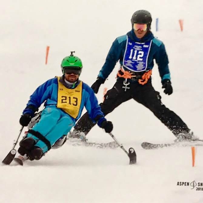 Mike carving through the snow on an adaptive sit-ski while his instructor skis alongside him at the National Disabled Veterans Winter Sports Clinic in Aspen
